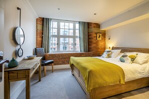 A bedroom with a wooden bed, a window with a view of buildings, a desk with a chair, and a mirror on the wall. - Cocoa Suites 37 - York city centre 1 bed apartment with sofa bed (sleeps 3) (York)