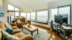 A spacious living room with a large window seat overlooking the sea, a television, and a wooden coffee table. - 'Rahus Ocean Refuge' with Manchester Coast Views! (Manchester)