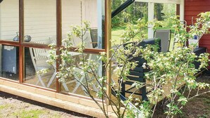 Ein überdachter Außenbereich mit Holzboden, Grill und Blick auf einen Garten.