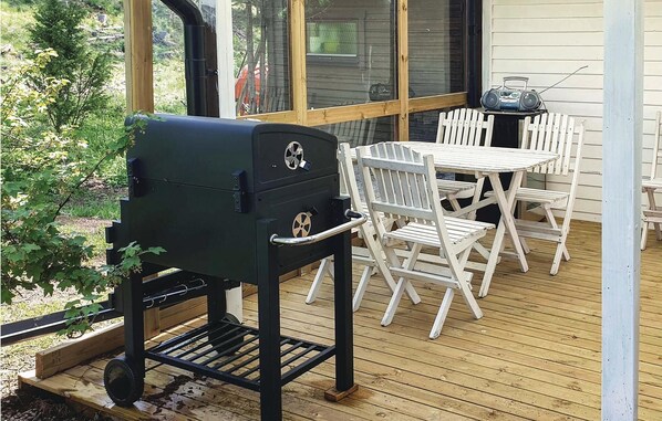 Une terrasse avec un barbecue, des chaises blanches et une table.