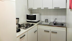 Ett kompakt kök med vita skåp, en mikrovågsugn, en vattenkokare, ett handfat och en brödrost.