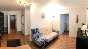 Ett kompakt vardagsrum med en soffa, ett matbord, ett litet sidobord, en lampa, en klocka och en garderob.
