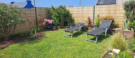 Un patio trasero con césped, tres sillas de jardín y diversas plantas.