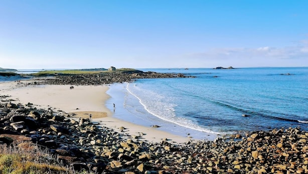 Ein felsiger Strand mit freiem Blick auf das Meer und ferne Hügel.