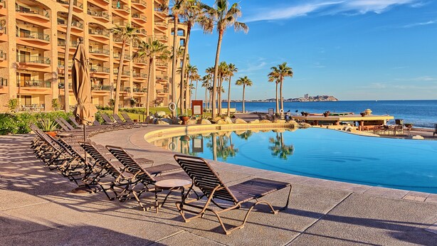 A hotel with a pool, lounge chairs, palm trees, and a view of the ocean. - Sonoran Sea E-804 Oceanfront Condo (Puerto Peñasco)