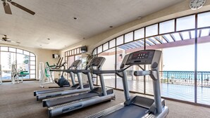 A gym with treadmills, exercise bikes, and a large window overlooking a balcony. - Sonoran Sea E-804 Oceanfront Condo (Puerto Peñasco)
