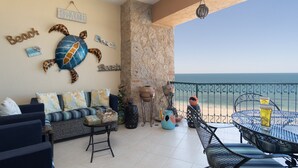 A balcony with a view of the sea, featuring a sofa, a table, and decorative items including a turtle mural and beach-themed decor. - Sonoran Sea E-804 Oceanfront Condo (Puerto Peñasco)