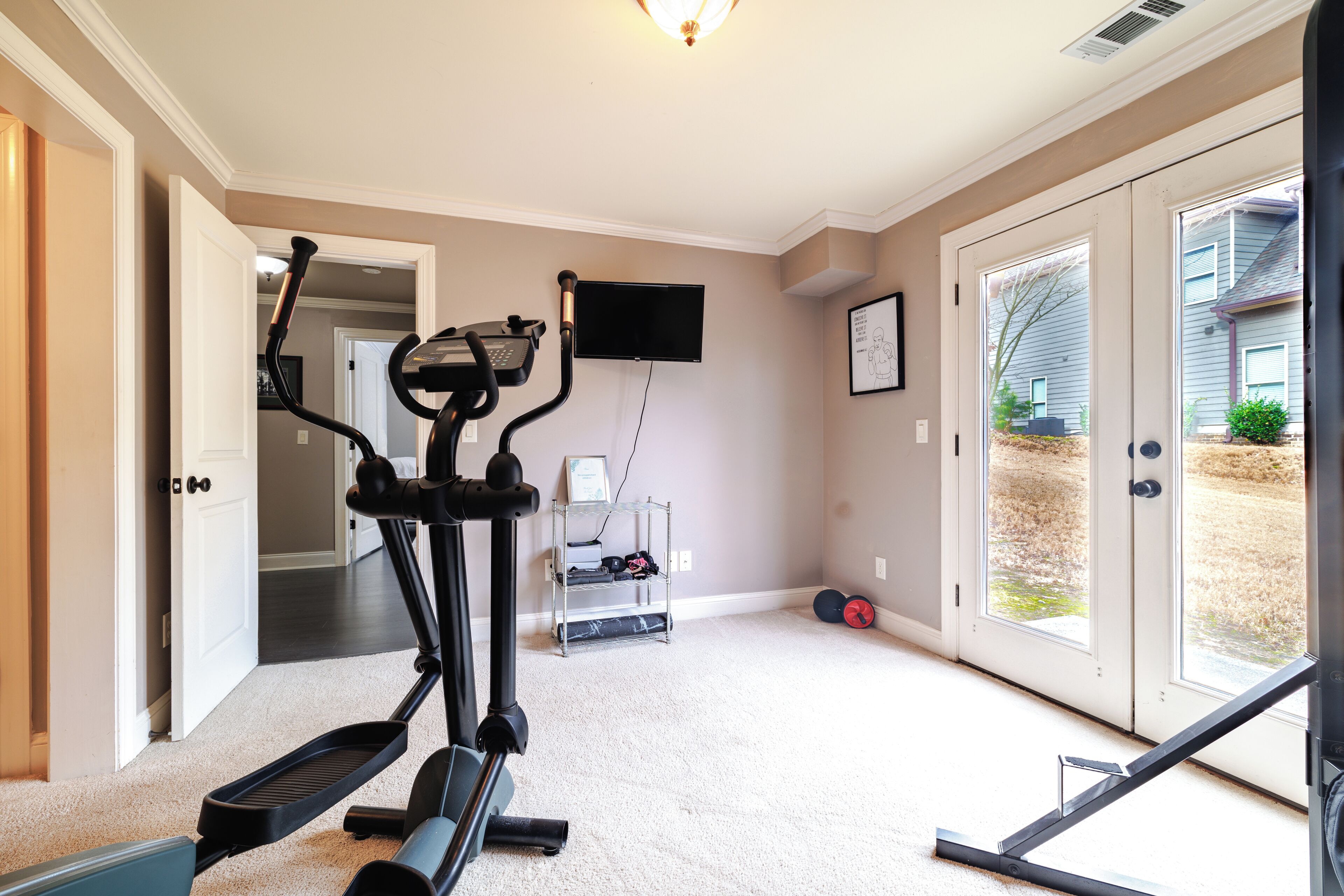 Une salle de sport à domicile équipée d’un vélo elliptique, d’un tapis de course et d’un banc de musculation.