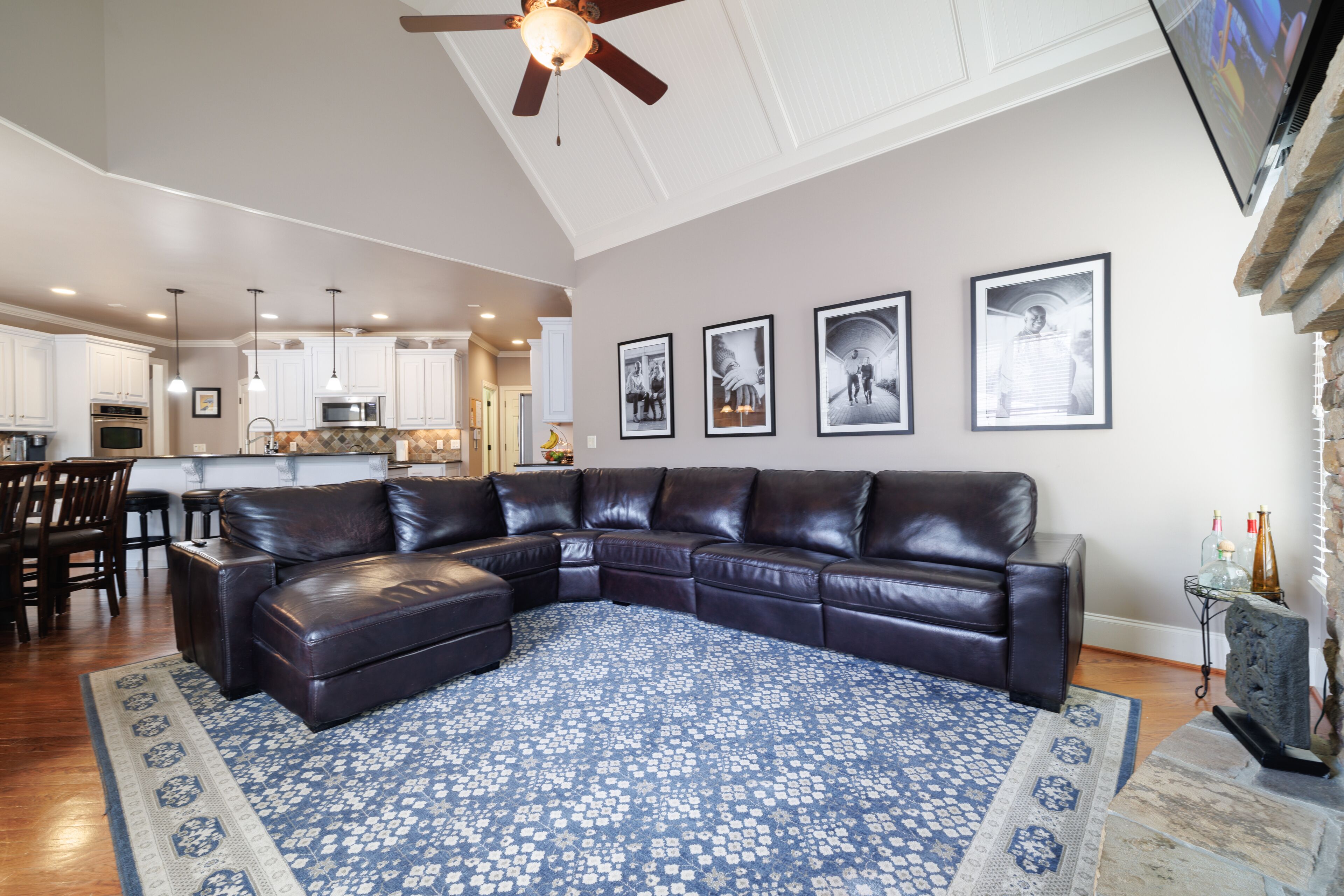 A spacious living room with a sectional sofa, a patterned rug, and a kitchen in the background.