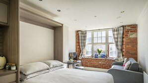 A hotel room with a large bed, a small table with a bottle and glasses, a sofa, and a window with curtains. - Cocoa Suites 35 - York city centre studio (with parking) - sleeps 3 (York)