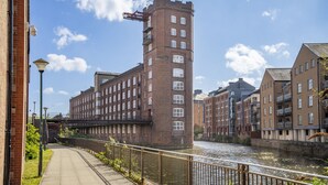 A riverside walkway with a brick building, a bridge, and adjacent residential buildings. - Cocoa Suites 35 - York city centre studio (with parking) - sleeps 3 (York)