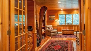 A cozy cabin interior with wooden walls, a large window, a leather chair, and a patterned rug.