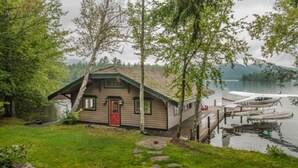 A cabin by a lake with a dock and a small boat.