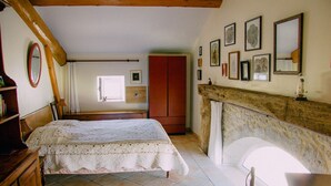 A bedroom with a bed, wooden wardrobe, and a stone fireplace. - Welcome to our house, we are happy to open its doors to you! (Calignac)