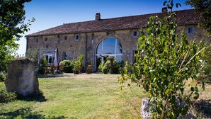 A stone building with a large arched window, a grassy yard, and outdoor seating. - Welcome to our house, we are happy to open its doors to you! (Calignac)