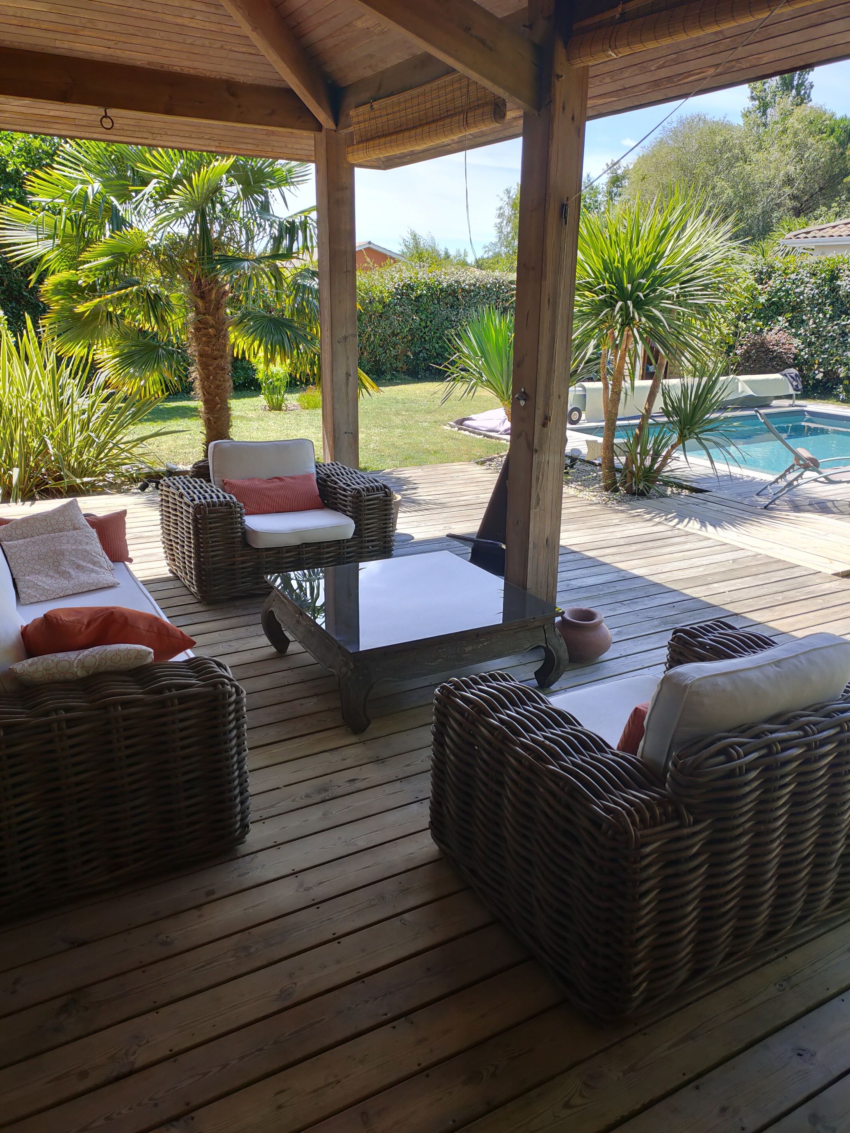An outdoor patio with wicker furniture, a glass-top table, and a view of a swimming pool.