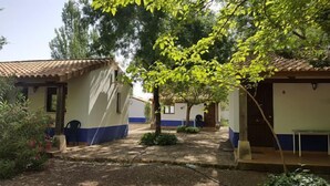 A courtyard with several small buildings, each with a tiled roof and a single door. There are trees and shrubs in the foreground, and a clear sky above. - Self catering Complejo Los Arenales for 4 people (Almagro)