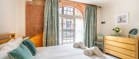 A bedroom with a large bed, a wooden dresser, a chair, and a window with curtains.