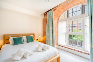 A hotel room with a large bed, a window with curtains, and a view of buildings outside.