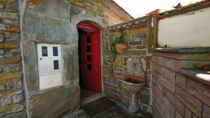 Un edificio de piedra con puerta roja, un cuadro eléctrico blanco y una jardinera de piedra.