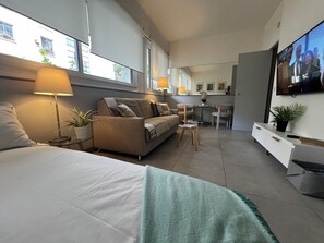 A modern living room with a sofa, a dining table, and a TV mounted on the wall.
