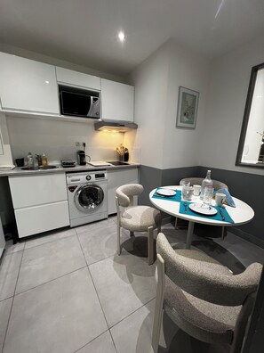 Cocina funcional con microondas, lavabo y lavadora. Cuenta con una mesa de comedor con sillas y un ventanal pequeño.