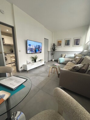 A modern living room with a flat-screen TV, a sofa, a coffee table, and a dining area with a glass table.