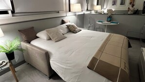 Una camera d'albergo moderna con un letto grande, un comodino con una lampada, una scrivania e una pianta in vaso.