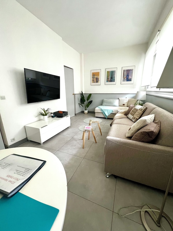 Una sala de estar moderna con una televisión de pantalla plana montada en la pared, un sofá, una mesa de centro y una mesita auxiliar.