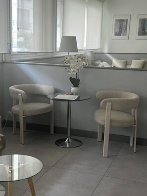 Habitación moderna con dos sillas, una mesita, una lámpara y una orquídea en maceta.