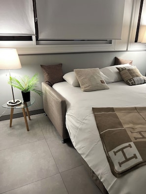 Un dormitorio moderno con cama, mesita de noche, lámpara y una planta en maceta.