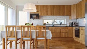 A modern kitchen with wooden cabinets, a dining area with a table and chairs, and a large window providing natural light.