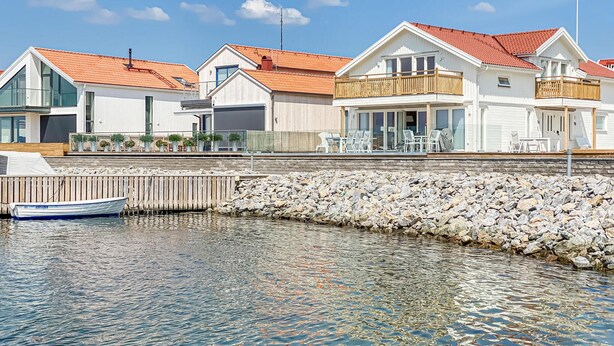 A waterfront property with a row of white houses, a wooden dock, and a rocky shoreline.