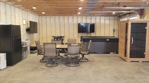 A compact kitchen with a refrigerator, a dining table with chairs, a television mounted on the wall, and a built-in grill.