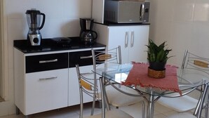 A compact kitchen with a black and white color scheme, a microwave, a coffee maker, and a blender on the countertop. There is a dining table with four chairs and a potted plant on it. - Vacation Home in Arraial do Cabo (Praia Grande)