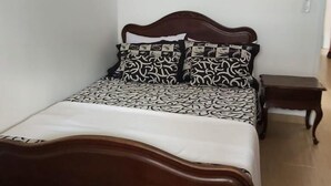A bedroom with a wooden bed, patterned bedding, a small bedside table, and a wall-mounted artwork of red flowers. - Vacation Home in Arraial do Cabo (Praia Grande)