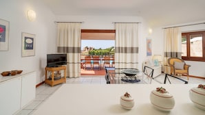 Un salón amplio con televisor, un comedor con sillas y una mesa, y vistas al exterior.