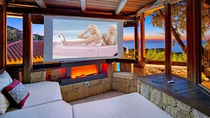 Un espacio exterior acogedor con chimenea de piedra, televisor de pantalla plana y vista al mar.