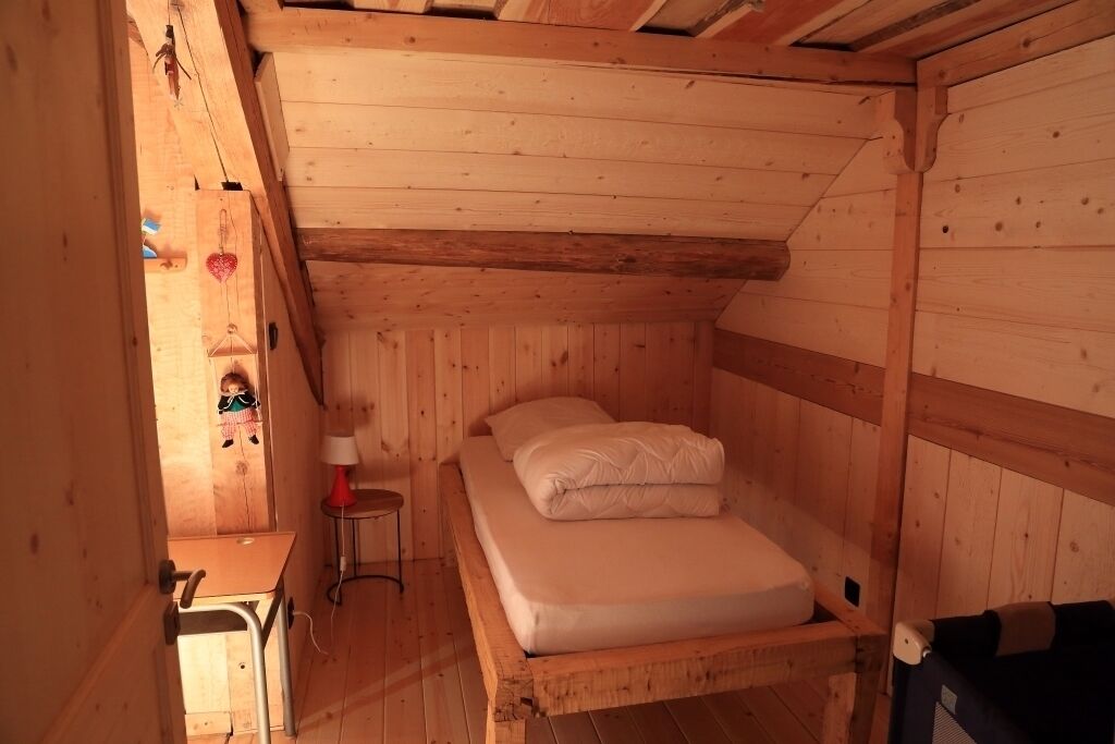 Een houten kamer met een bed, een klein tafeltje en een stoel.