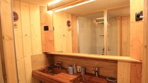 A wooden bathroom with two sinks, a large mirror, and a shower area.