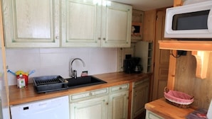 A kitchen with light green cabinets, a wooden countertop, a sink, a coffee maker, and a microwave.