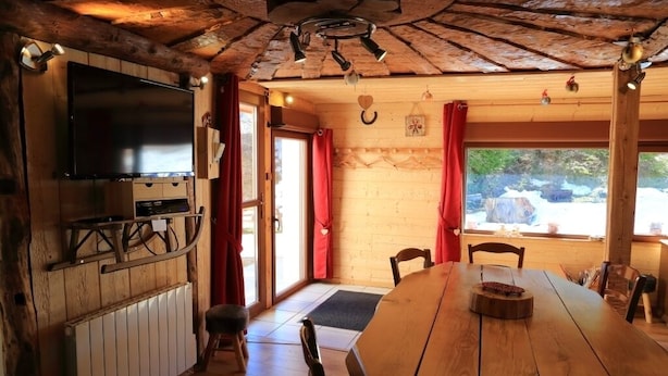 A wooden interior with a large table, chairs, a television, and a window with a view of the outdoors.