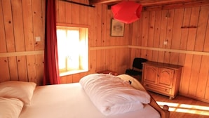 A wooden cabin room with a bed, a dresser, and a window letting in natural light.