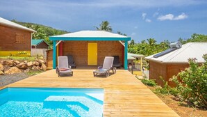 A wooden deck with a pool, two lounge chairs, and a small building with a blue roof. - ---- LOVE DESHAIES 2 --- (DESHAIES)