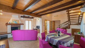 Amplia sala de estar con techo de madera, un sofá rosa, una mesa de comedor con sillas y una escalera.