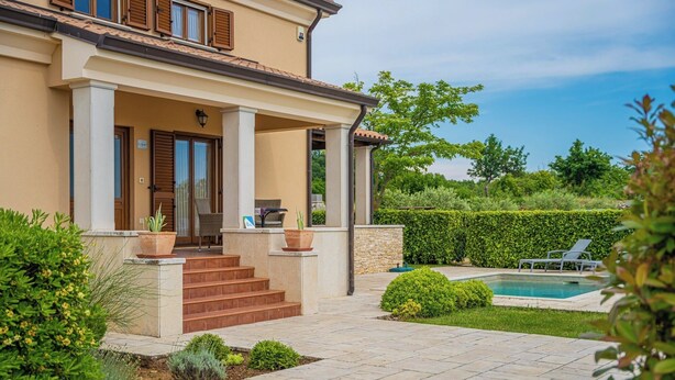 Una casa de dos pisos con un porche cubierto, una piscina y un jardín bien cuidado.