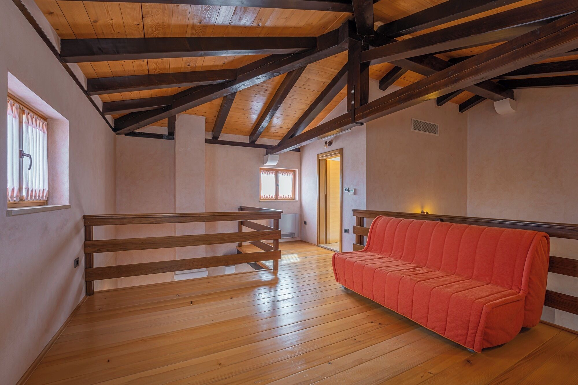 Um quarto amplo com vigas de madeira, um banco de madeira e um sofá vermelho.