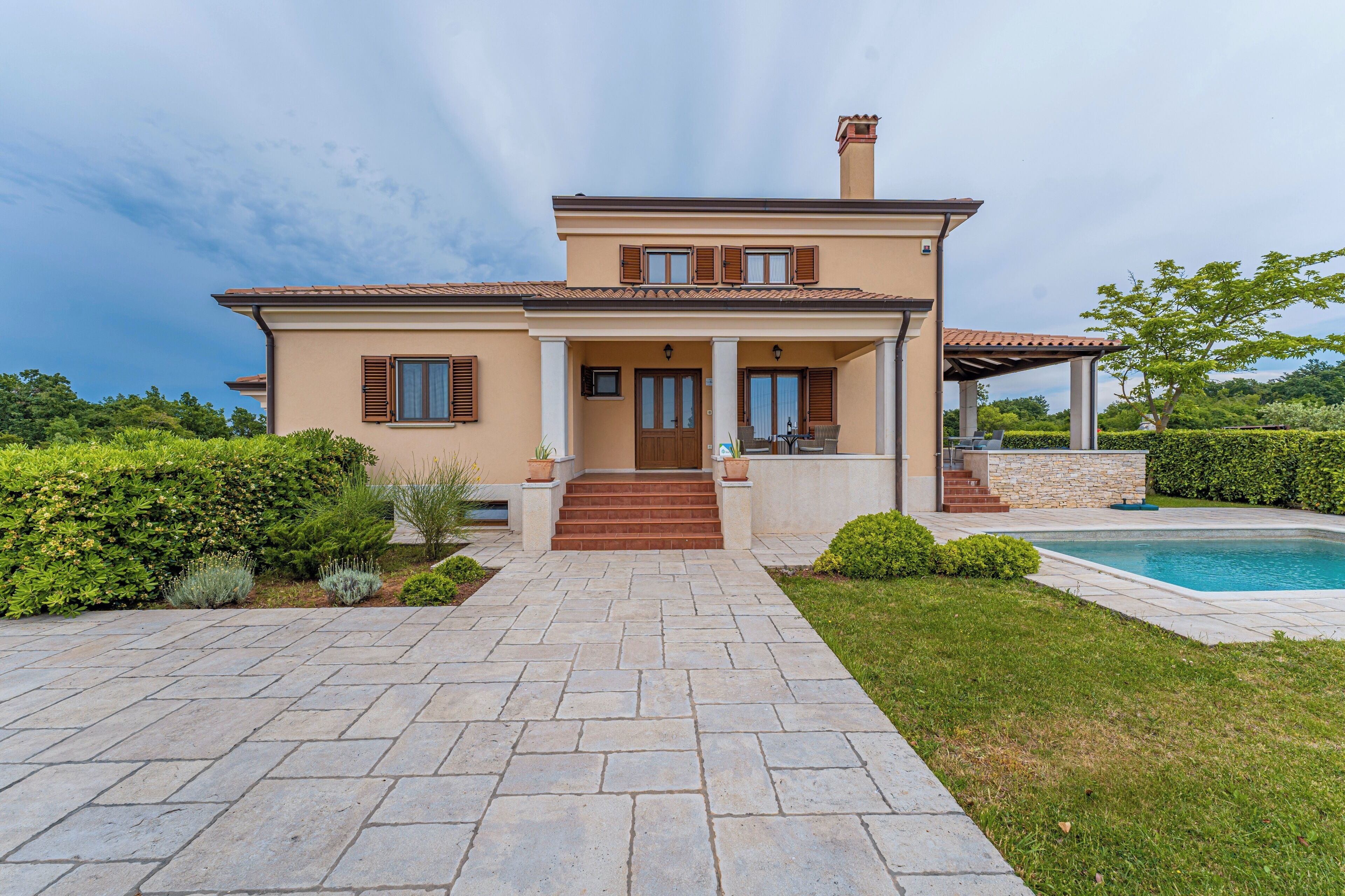 A two-story house with a stone pathway leading to the entrance, a swimming pool, and a well-maintained garden.