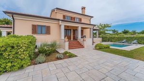 Una casa de dos pisos con piscina, un patio cubierto y un jardín bien cuidado.