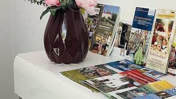 Ein weißer Tisch mit einer Vase voller pinkfarbener Blumen, Broschüren und einer Zeitschrift.